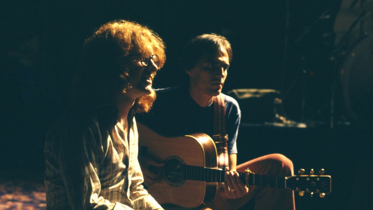 a man with a guitar next to a long haired man